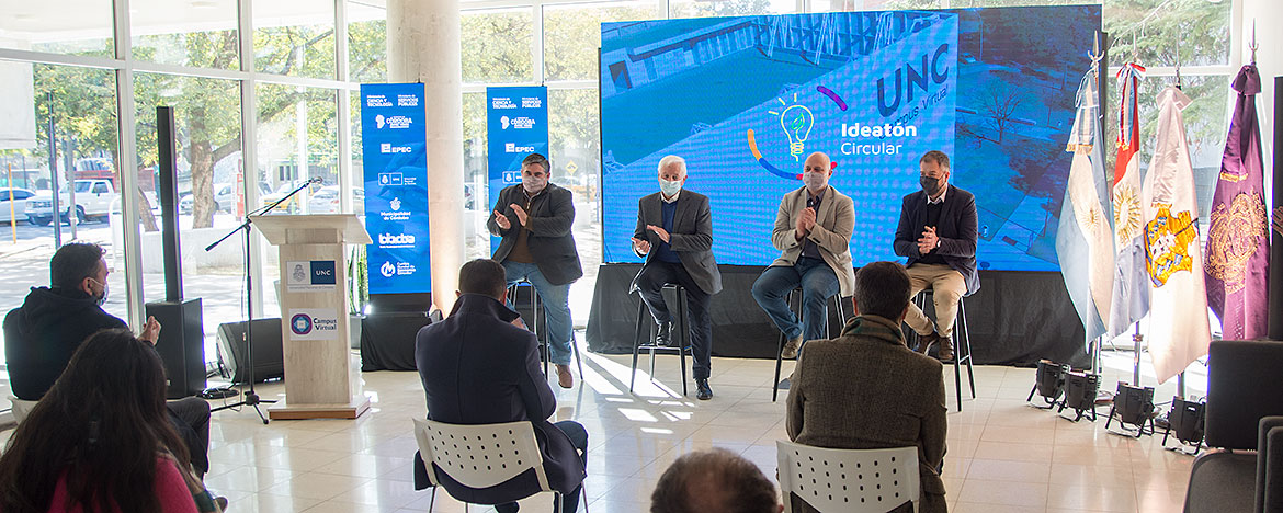 Aplaudiendo, Hugo Juri, Pablo de Chiara, Conrado Storani y Enzo Cravero están sentados en banquetas altas con una pantalla gigante detrás en un ambiente amplio cubierto por vidrios en un día soleado