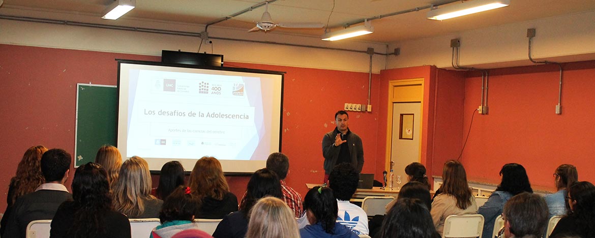 Un docente de pie explicando un tema frente a una treintena de estudiantes